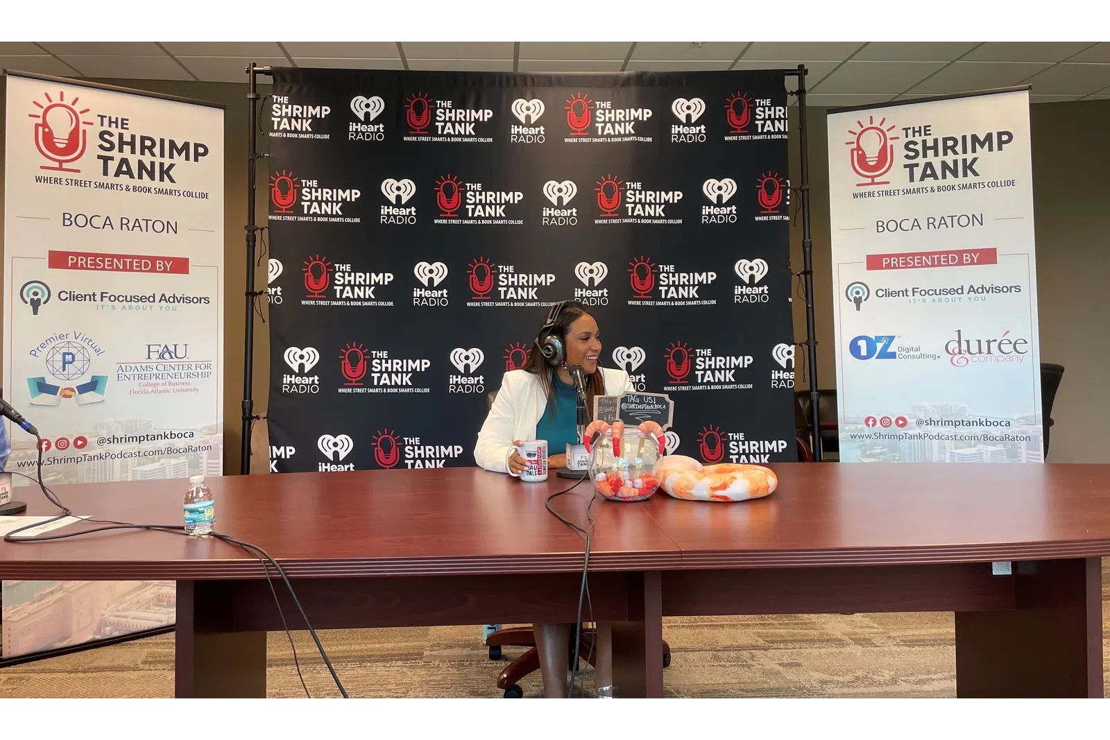 a person sitting at a table with a microphone and a sign behind the