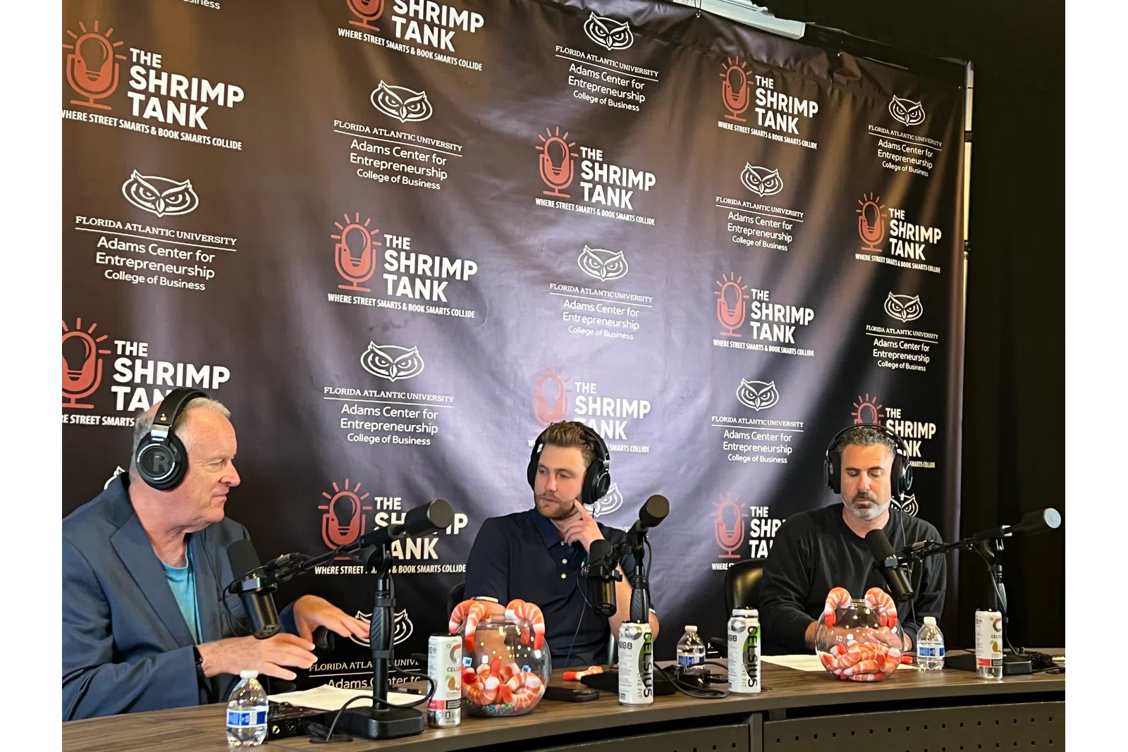 a group of men sitting at a table with microphones and a banner