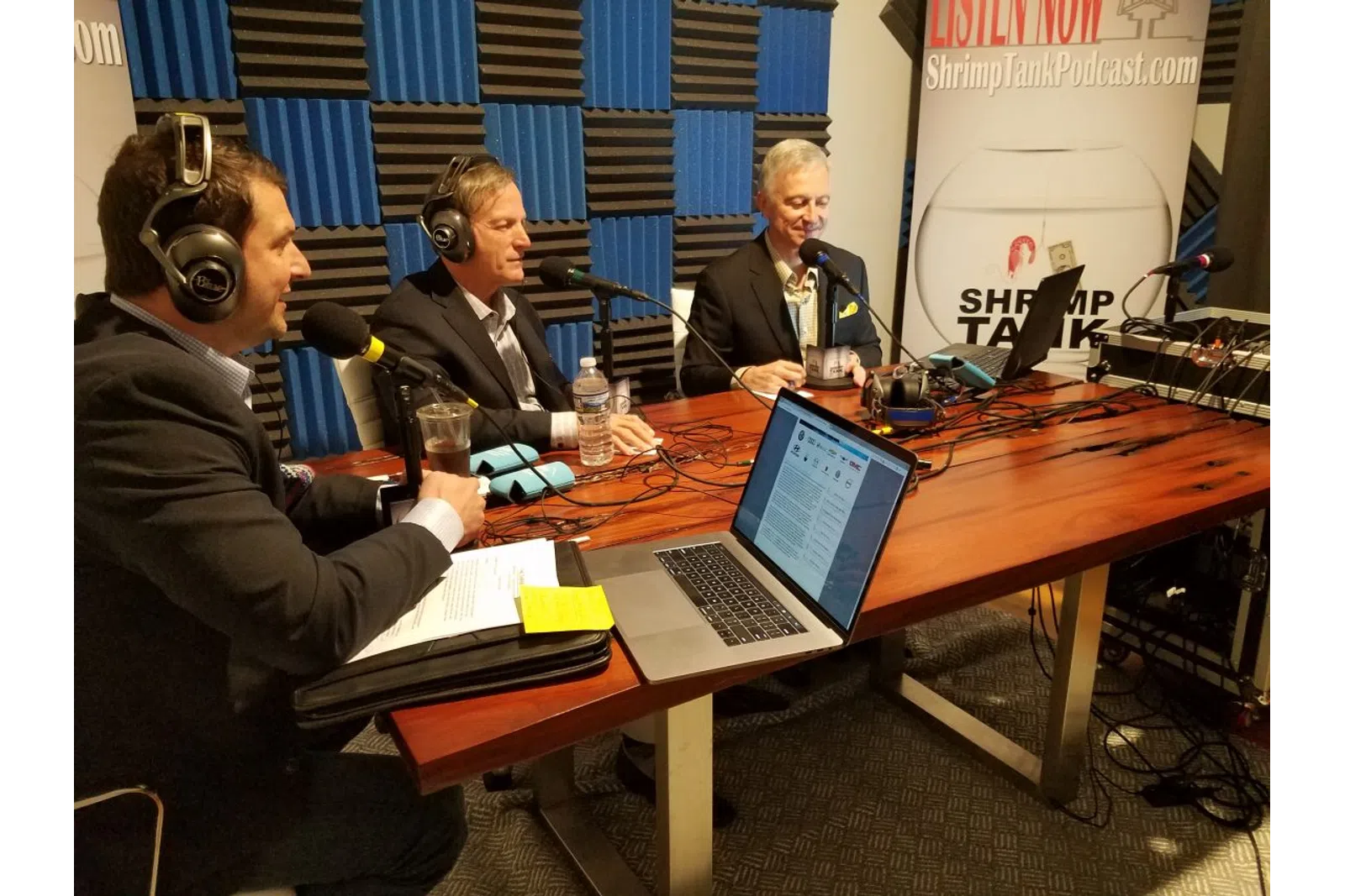 a group of men sitting at a table with laptops and microphones