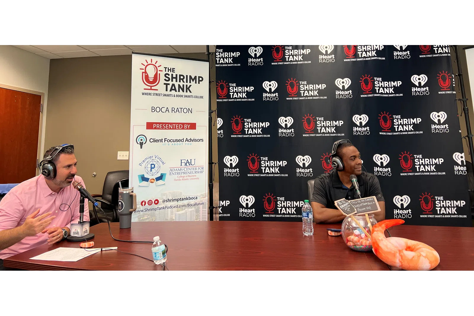 a couple of men sitting at a table with microphones and a sign