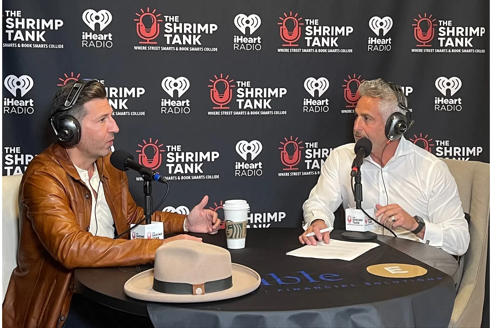 a couple of men wearing headphones and sitting at a table with a cake