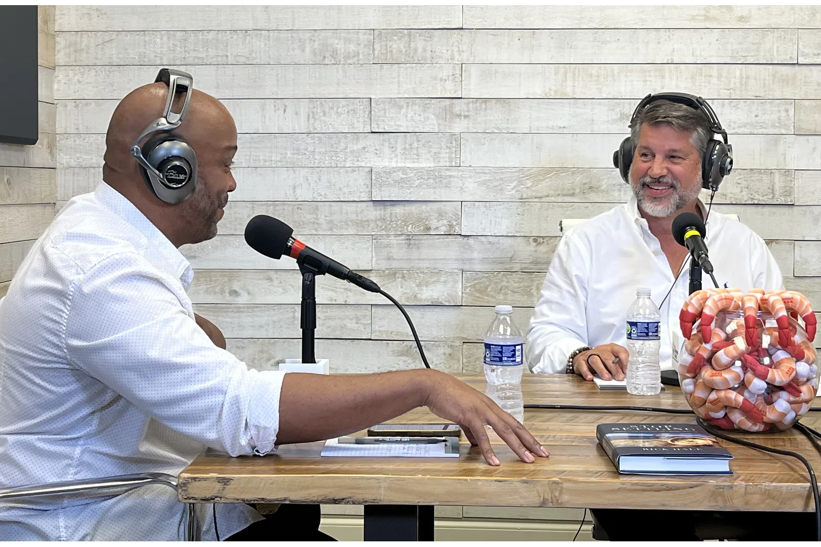a couple of men wearing headphones and sitting at a table with a microphone