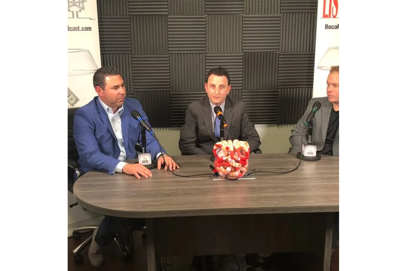 a group of men sitting at a table with a microphone and a basket of fruit