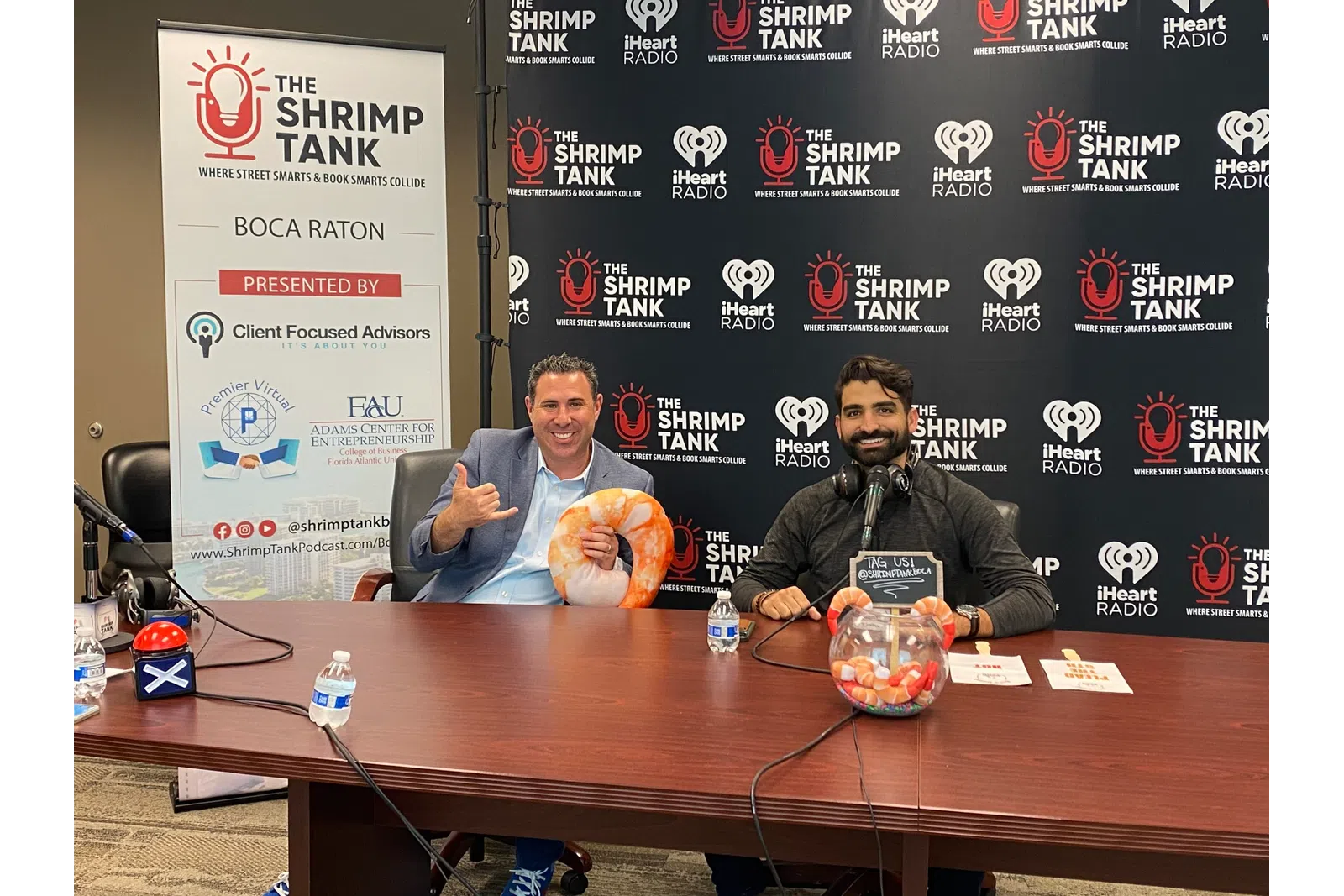 a couple of men sitting at a table with microphones and a sign behind them
