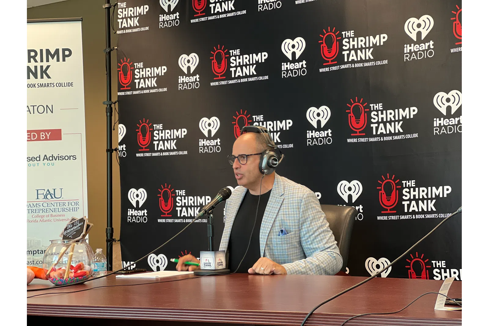 a person sitting at a desk with a microphone and a screen behind him