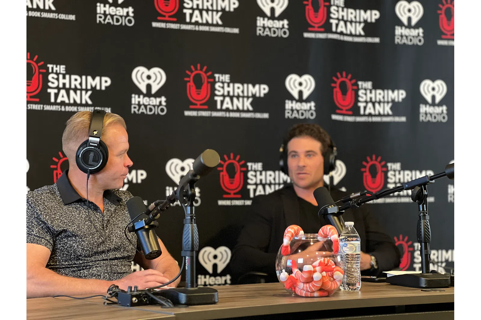 a couple of men wearing headphones and sitting at a table with microphones