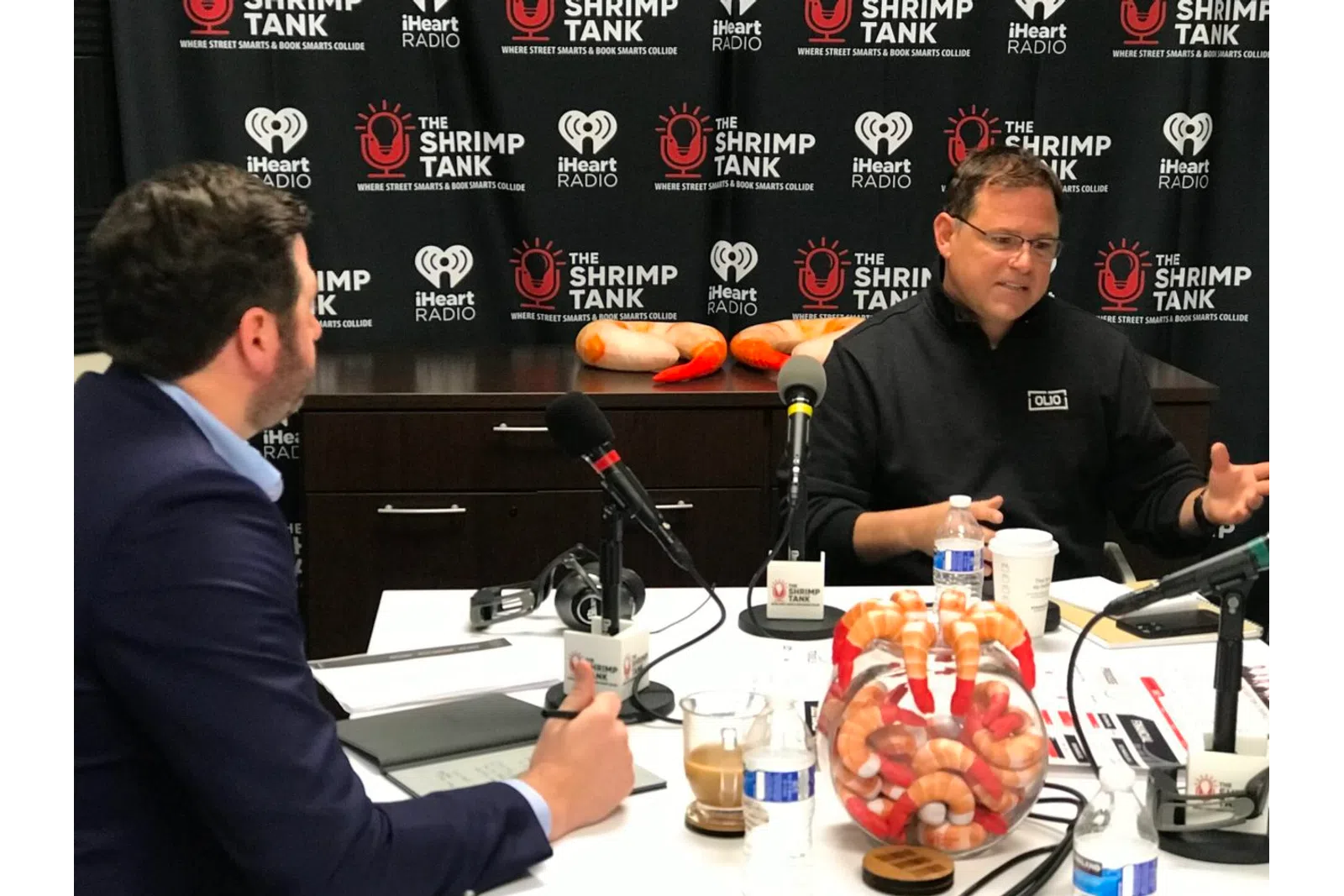 a person sitting at a table with a microphone and a person standing behind him
