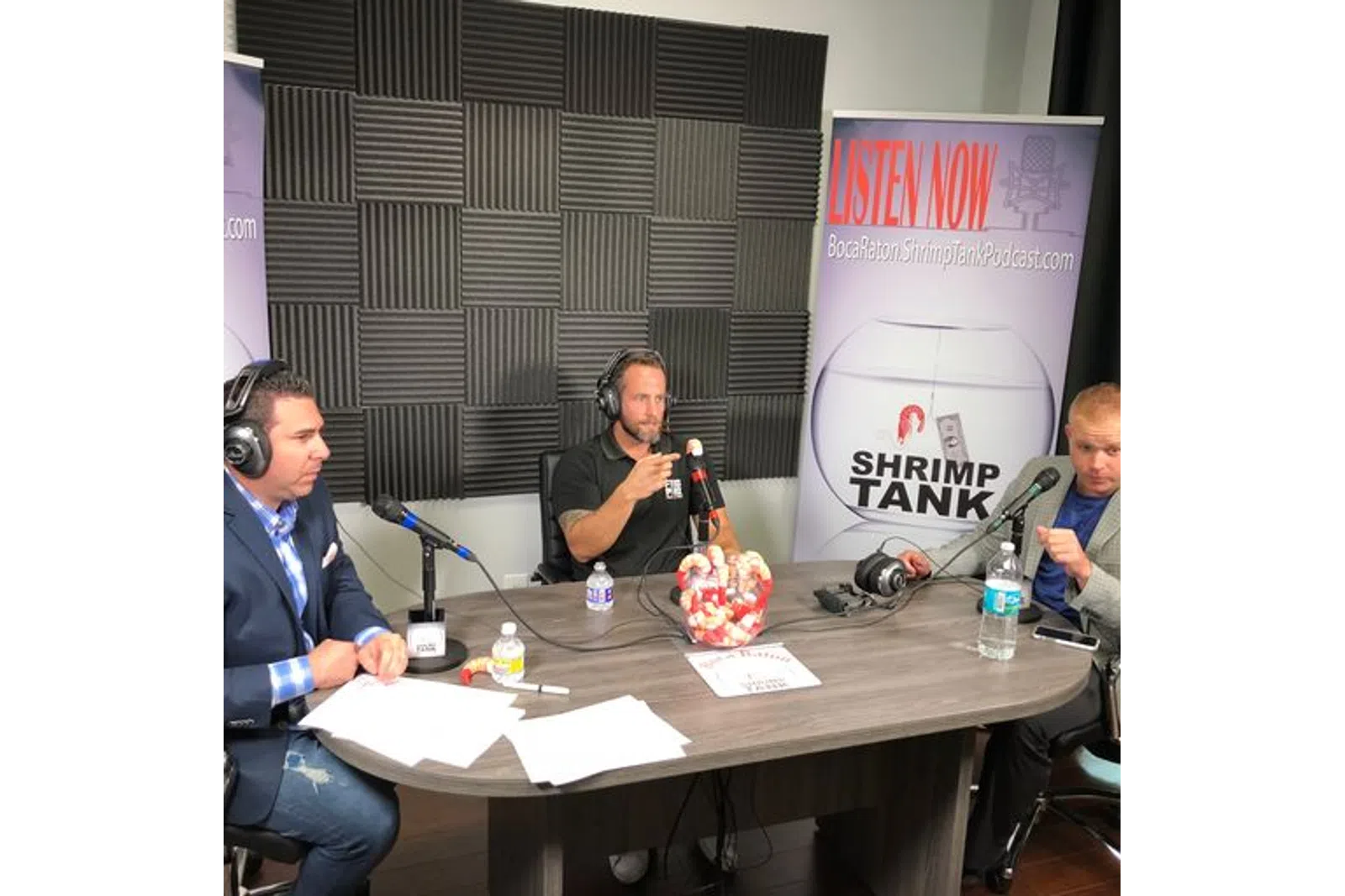 a group of men sitting at a table with microphones and a sign
