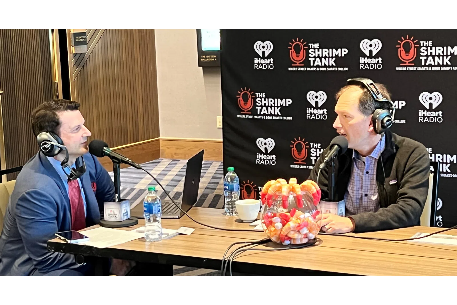 a couple of men sitting at a table with microphones and food