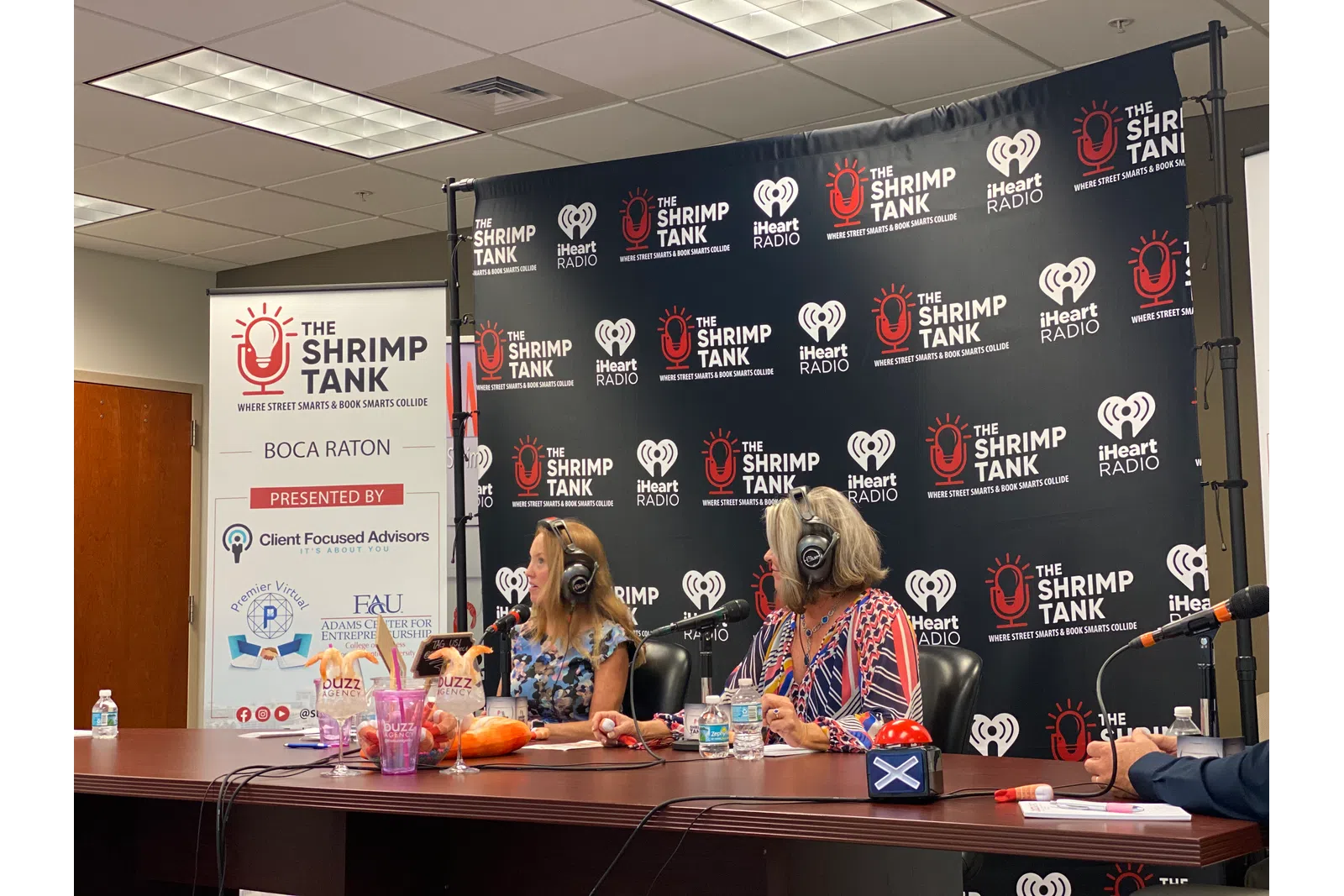 a couple of women sitting at a table with microphones and a large screen behind them