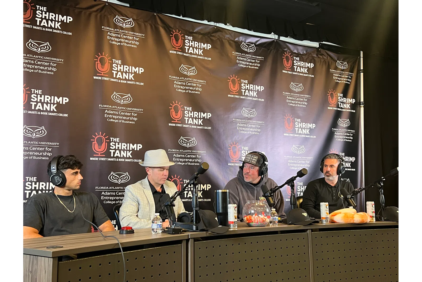 Four men seated at podcast table with microphones under The Shrimp Tank backdrop at Florida Atlantic University event.