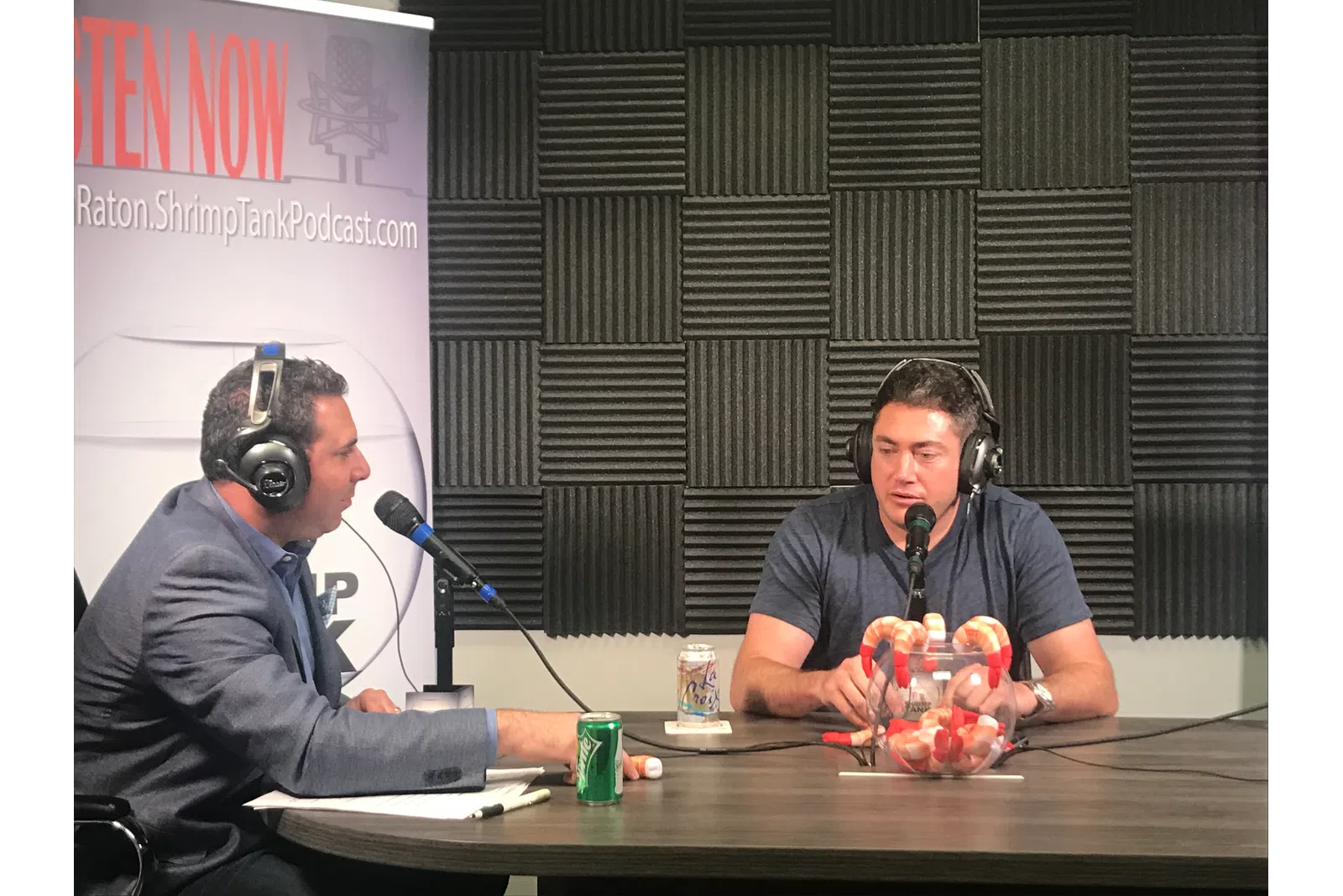 a couple of men sitting at a table with microphones and food