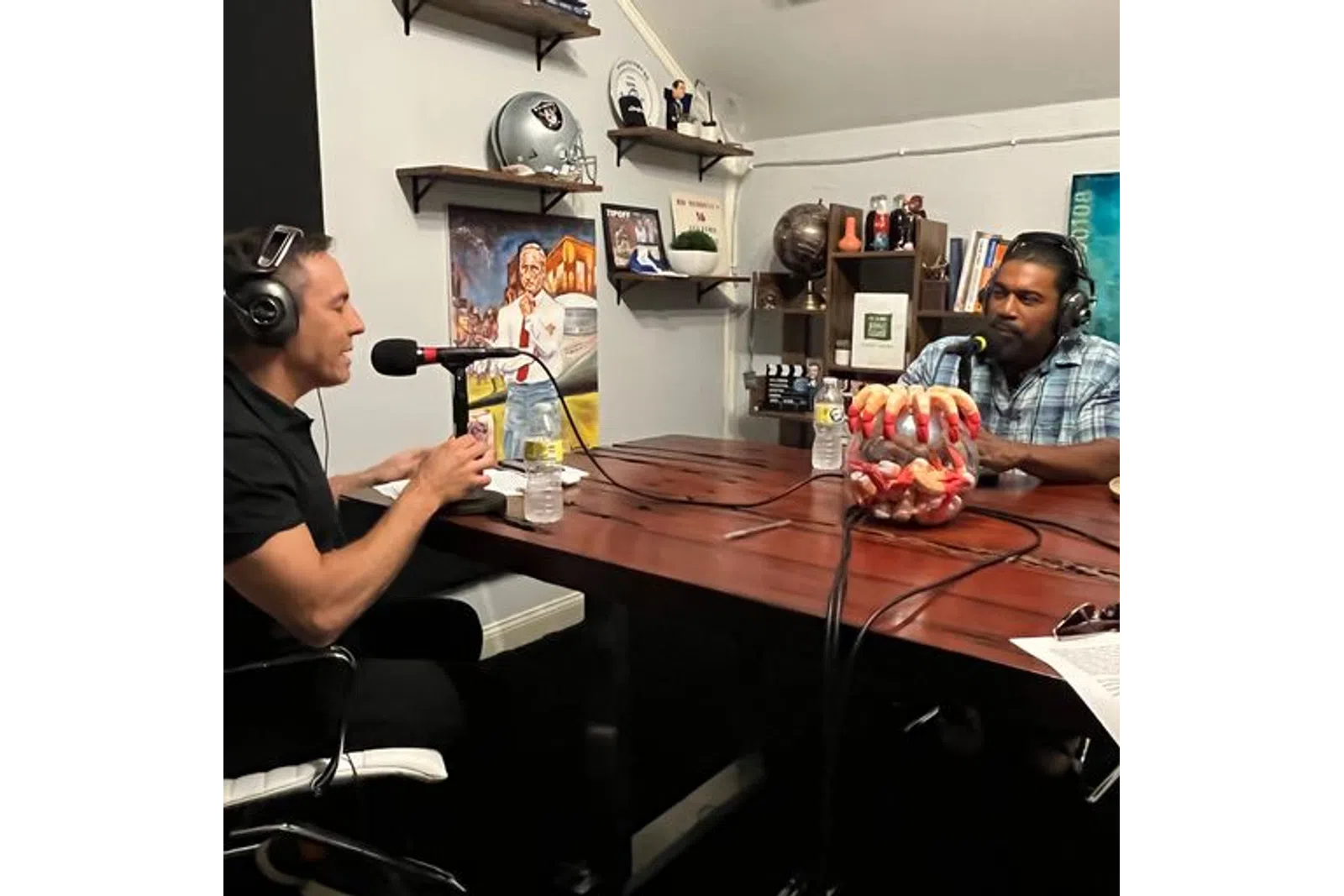 a couple of men sitting at a table with a microphone and a basket of fruit