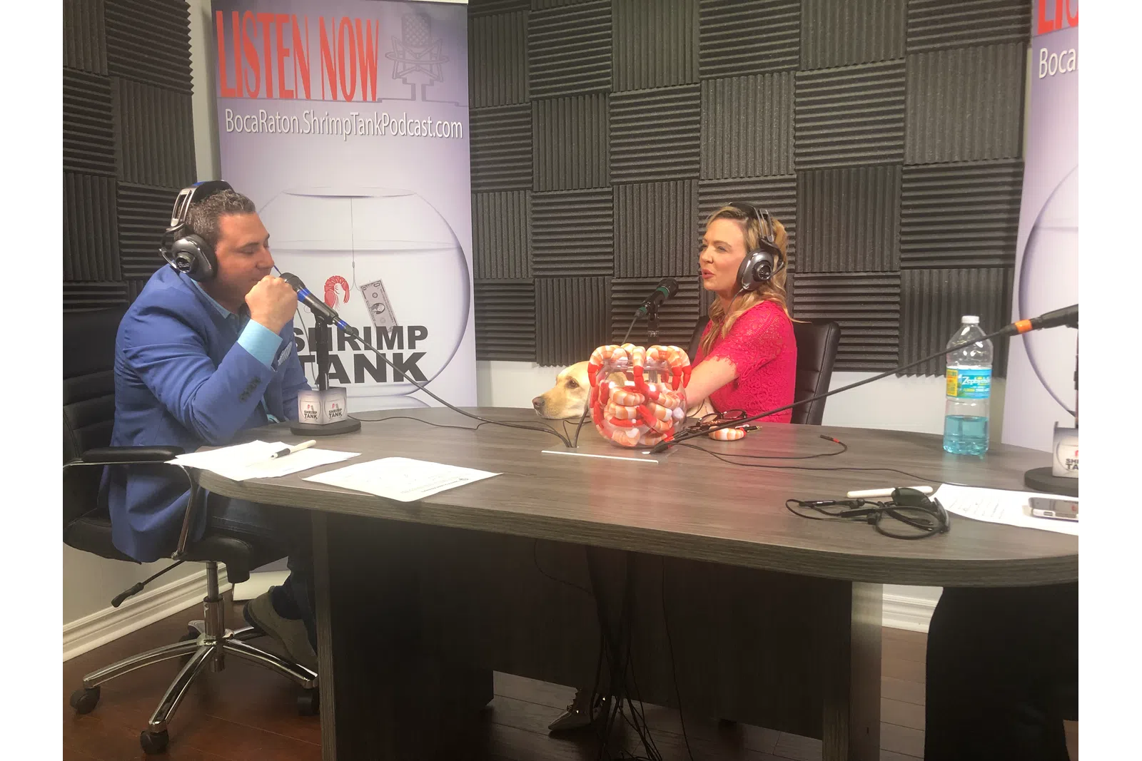 a man and woman sitting at a table with a microphone and a dog
