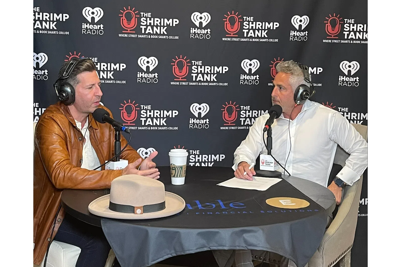 a man in a suit and headphones sitting at a table with a cake and microphones