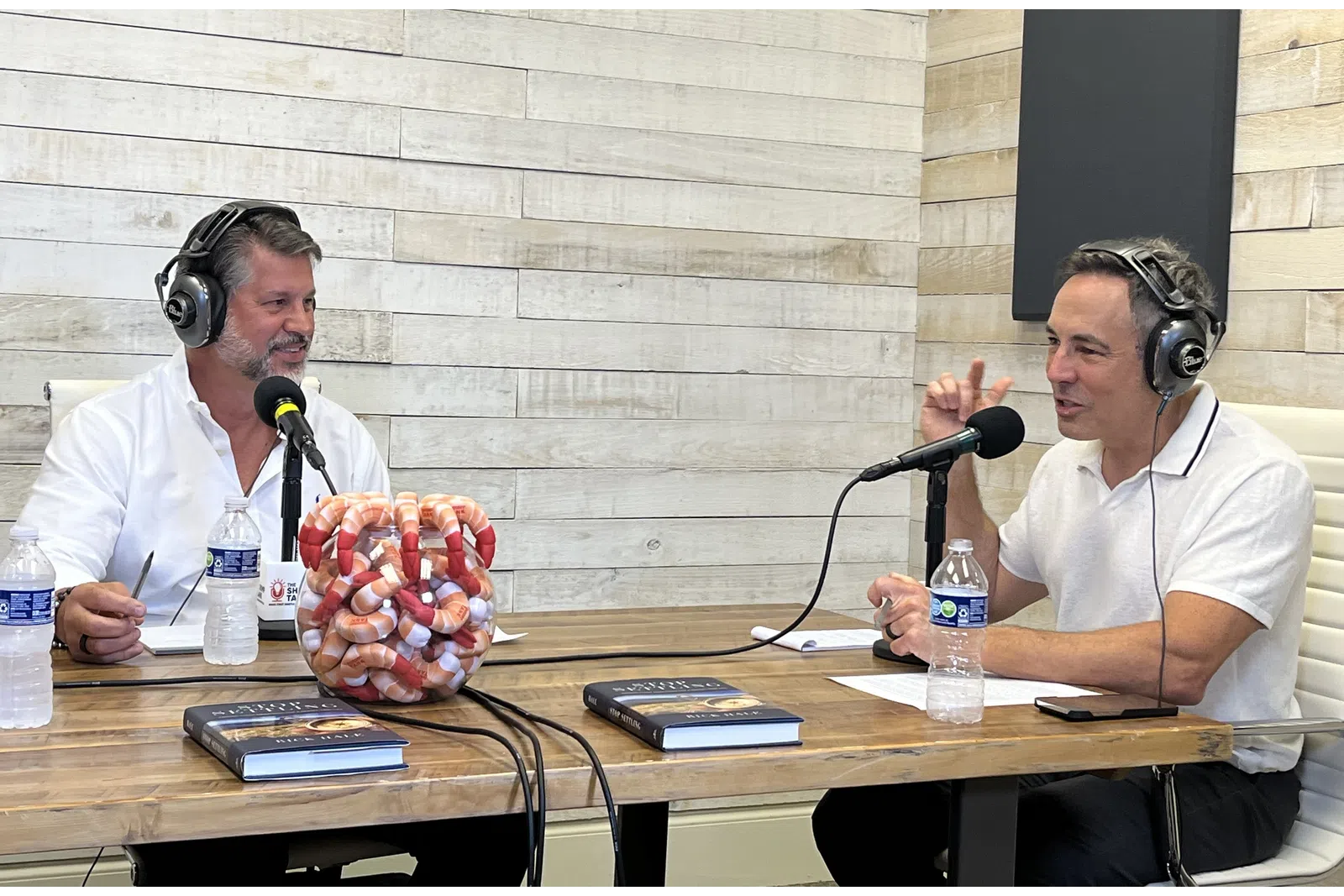 a couple of men sitting at a table with microphones and food