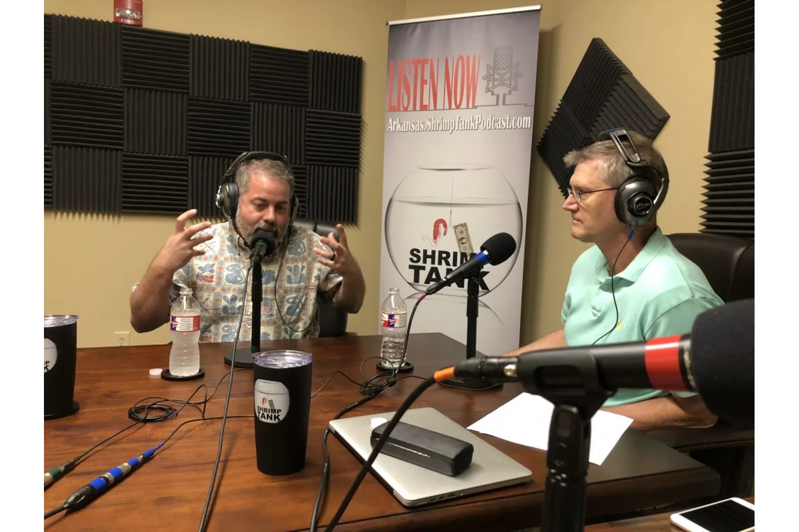 a man and woman sitting at a table with microphones and a sign