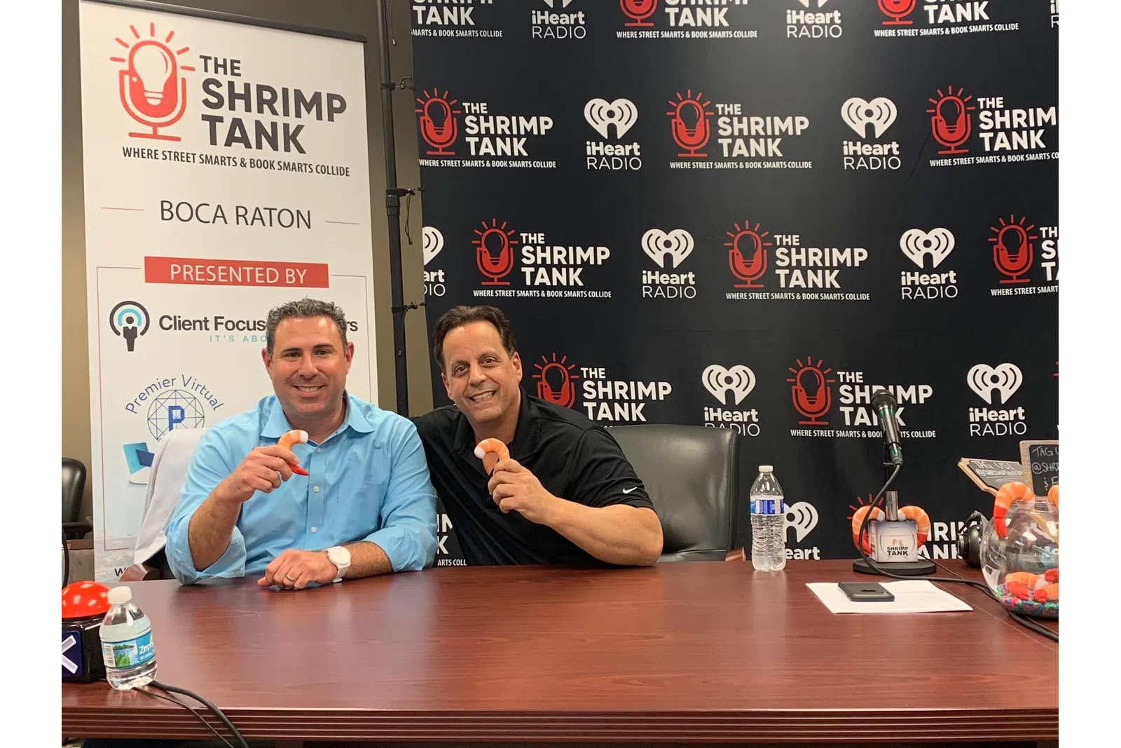 a couple of men sitting at a table with microphones and a sign behind them