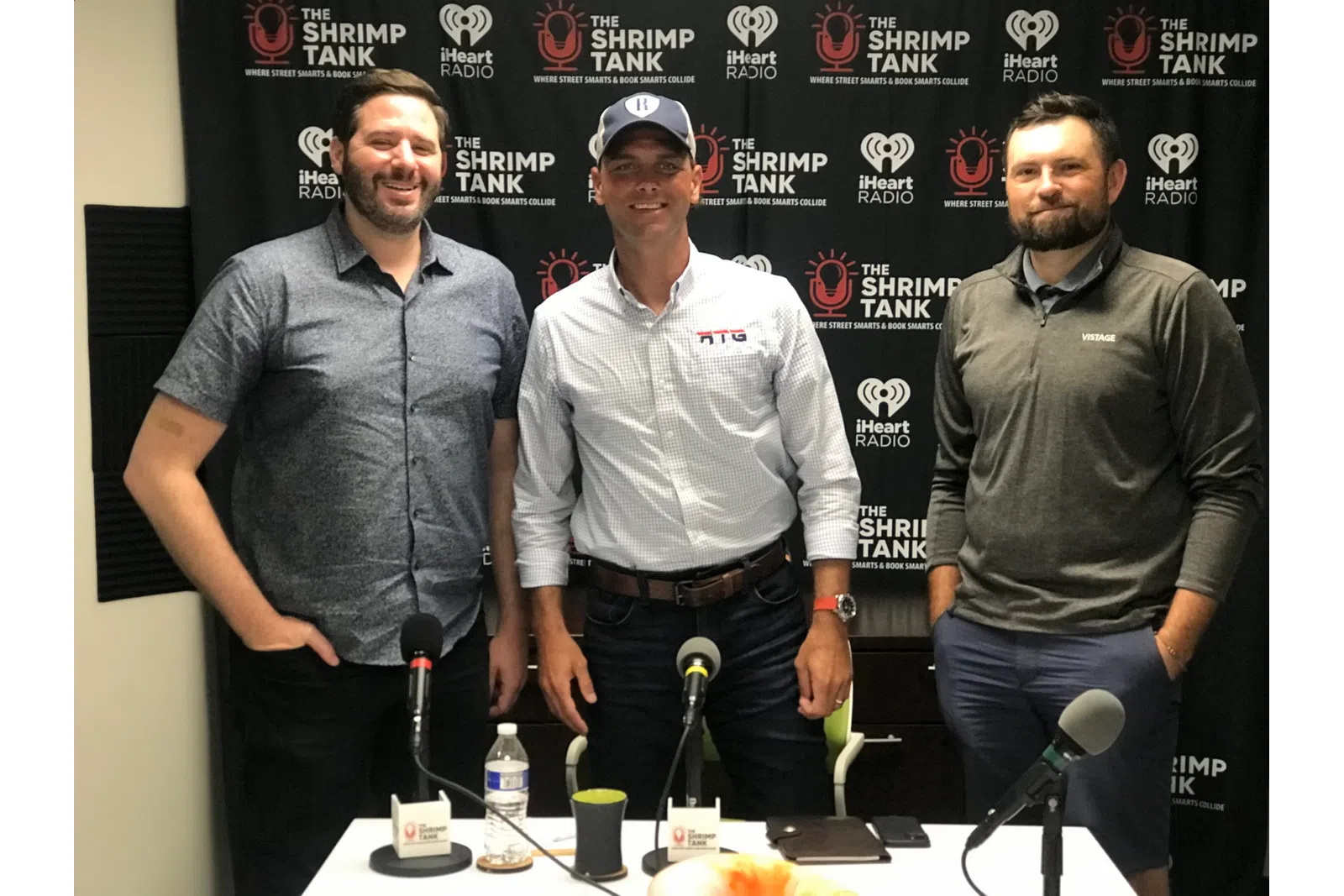 a group of men standing next to a table with microphones