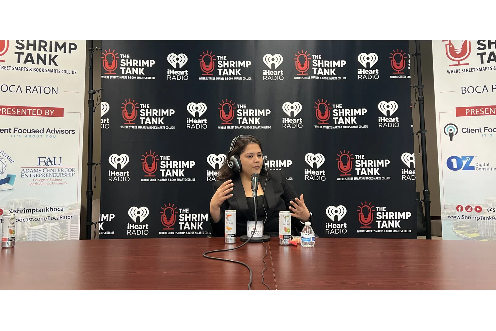 a person sitting at a table with a microphone and a sign behind the
