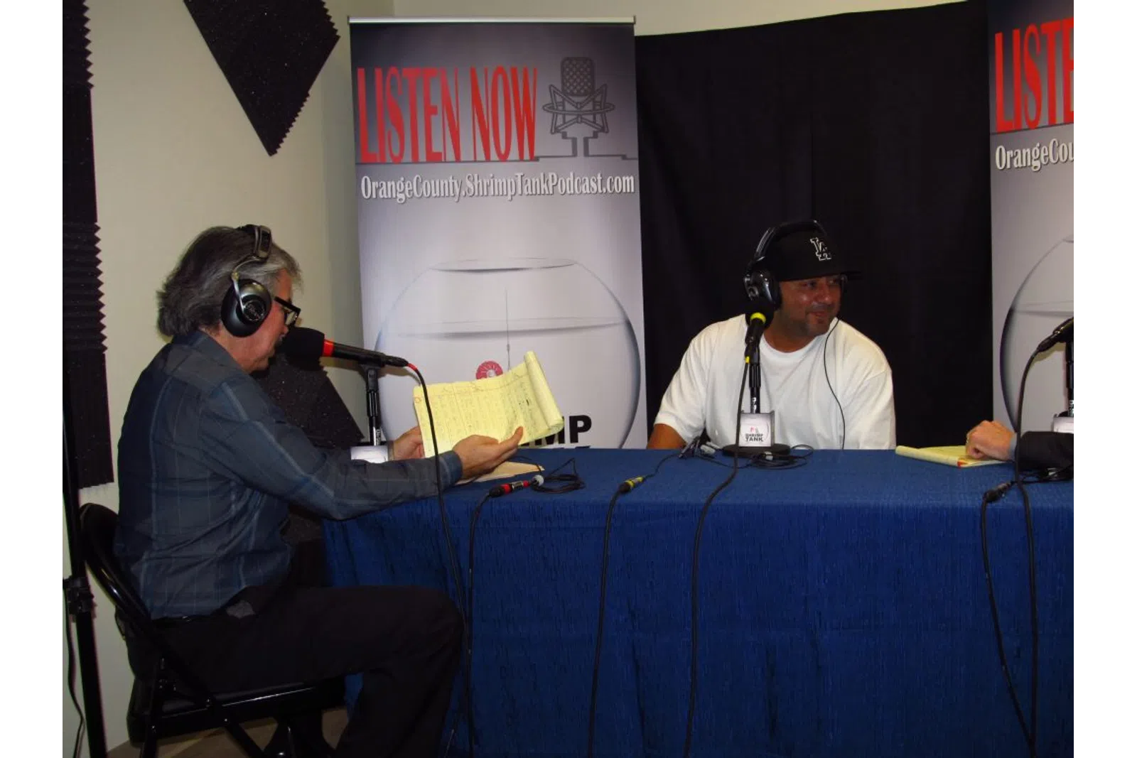 a man wearing headphones and sitting next to a man wearing a hat