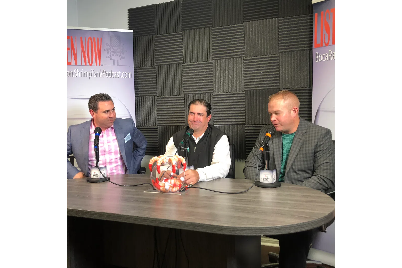 a group of men sitting at a table with microphones and food
