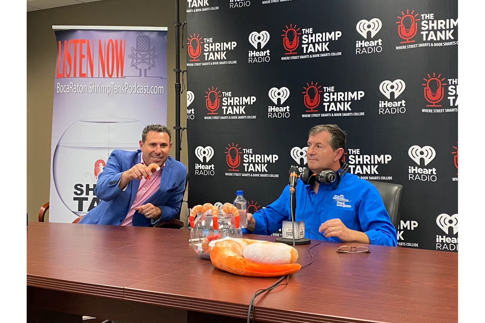 a couple of men sitting at a table with a microphone and a cake