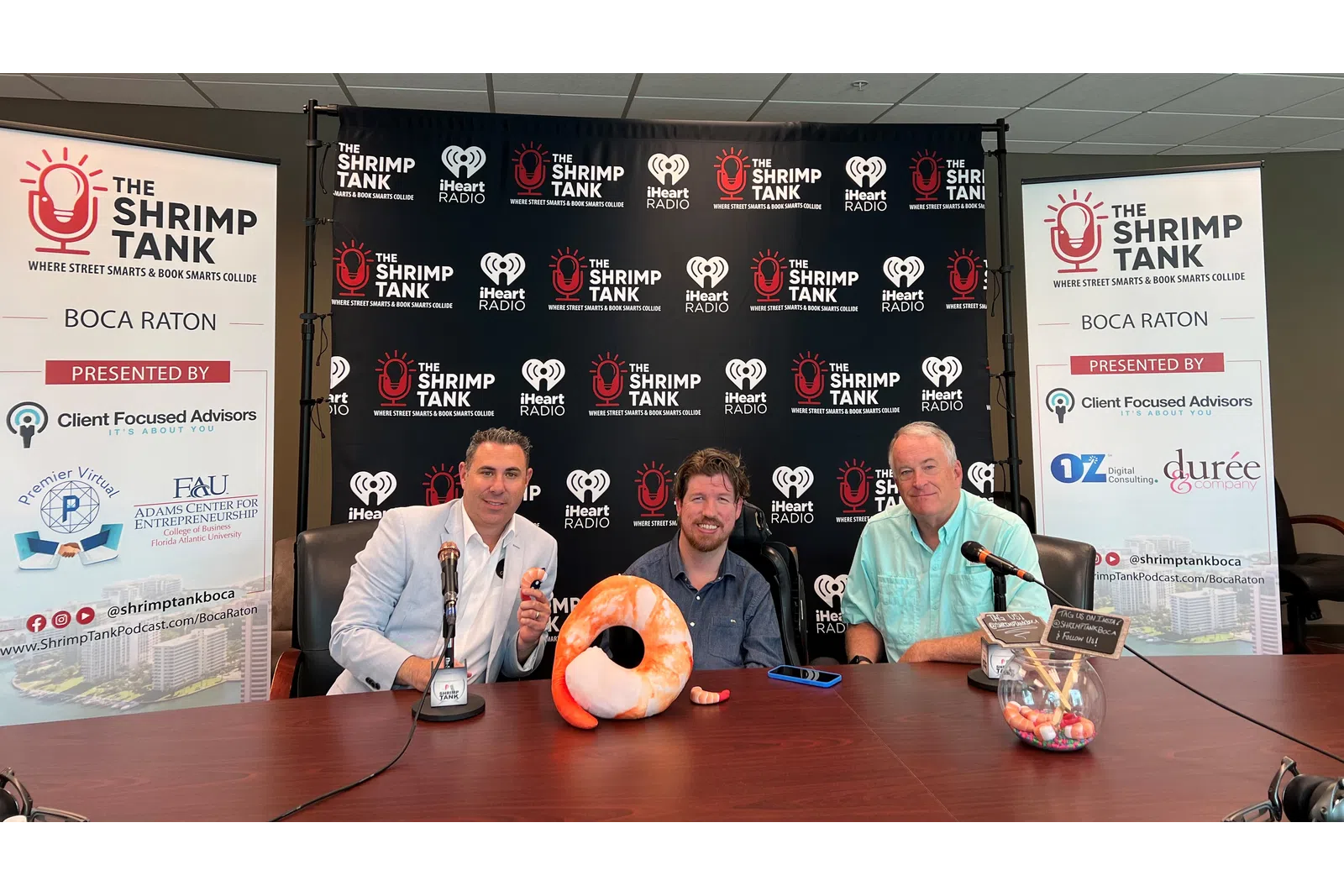 a group of men sitting at a table with microphones and a sign