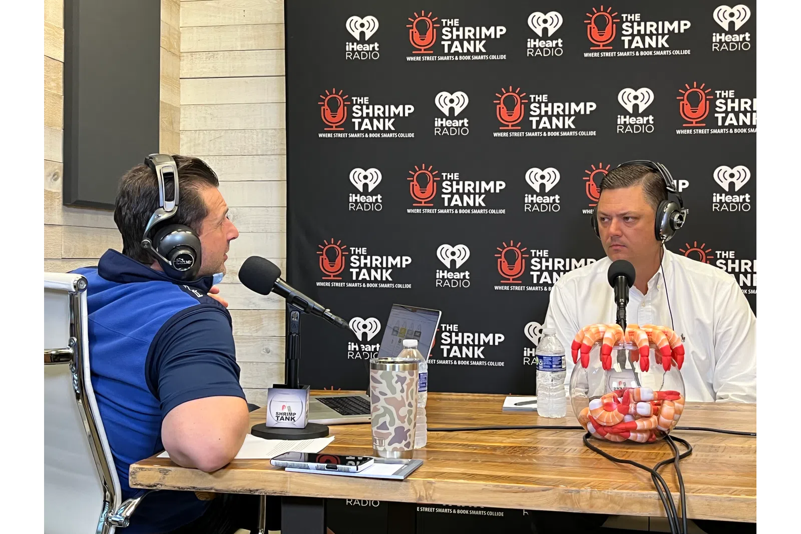 a couple of men wearing headphones and sitting at a table with microphones