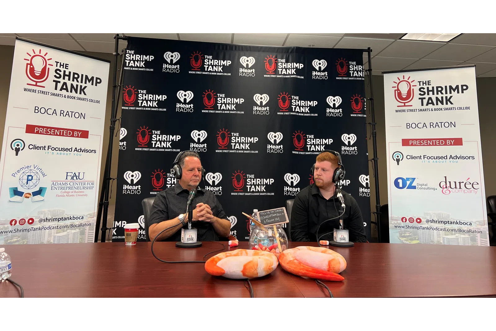 a couple of men sitting at a table with microphones and food
