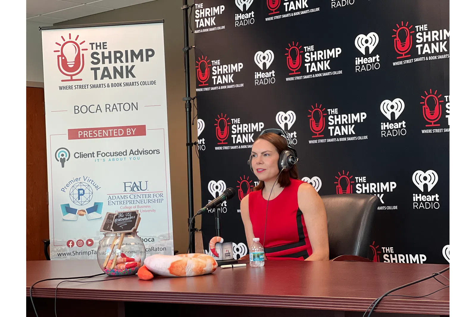 a person sitting at a table with a microphone and a sign behind the