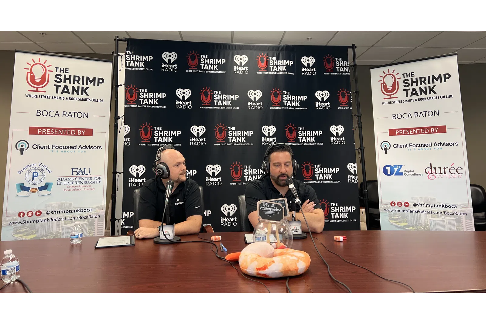 a couple of men sitting at a table with microphones and food