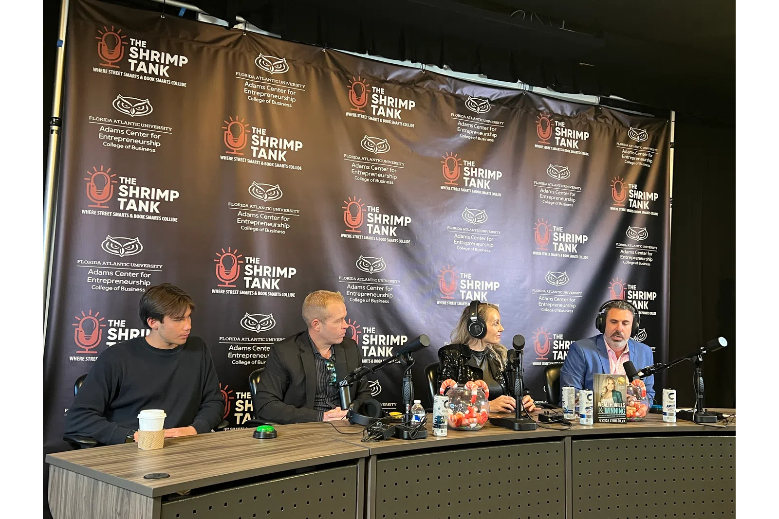 Four people seated at a table with microphones, recording a podcast or panel discussion at The Shrimp Tank event.