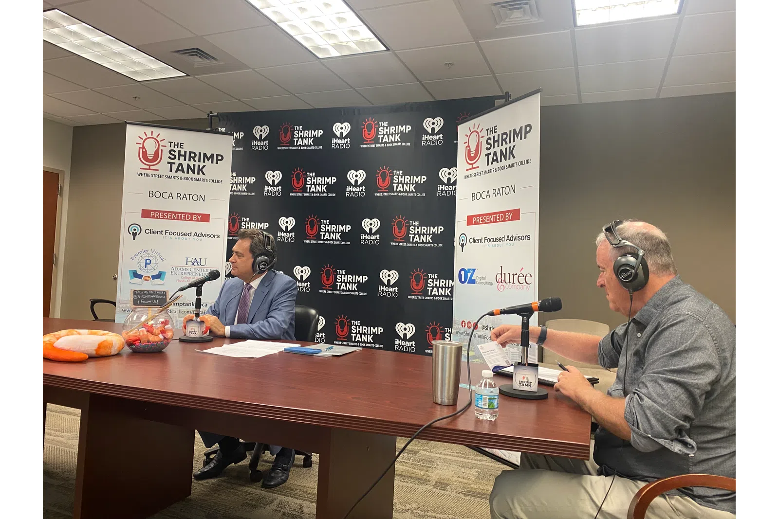 a couple of men sitting at a table with microphones and food