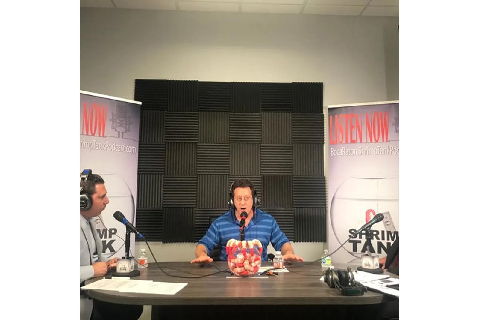 a man sitting at a desk with a microphone and a man standing behind him