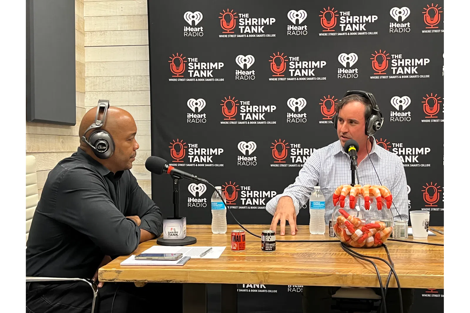 a couple of men wearing headphones and sitting at a table with microphones