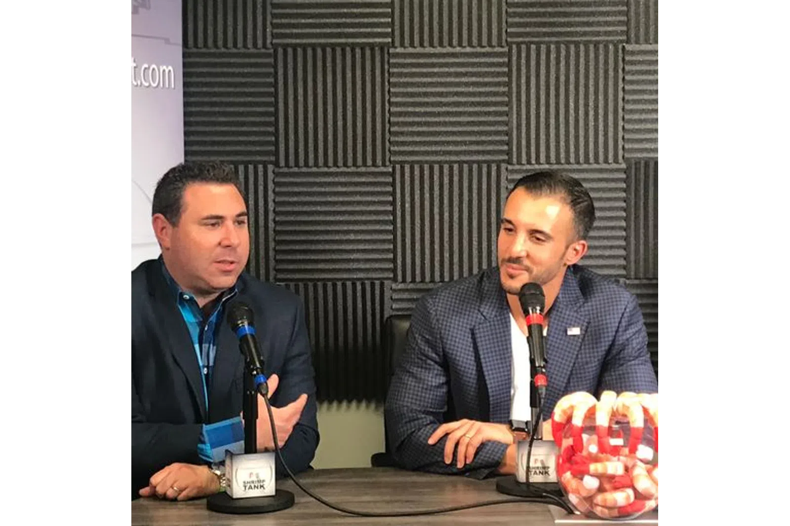 a couple of men sitting at a table with microphones and food