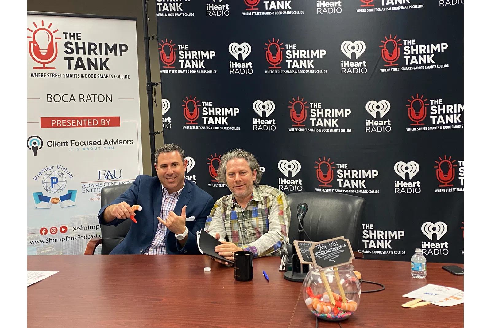 a couple of men sitting at a table with a sign behind them