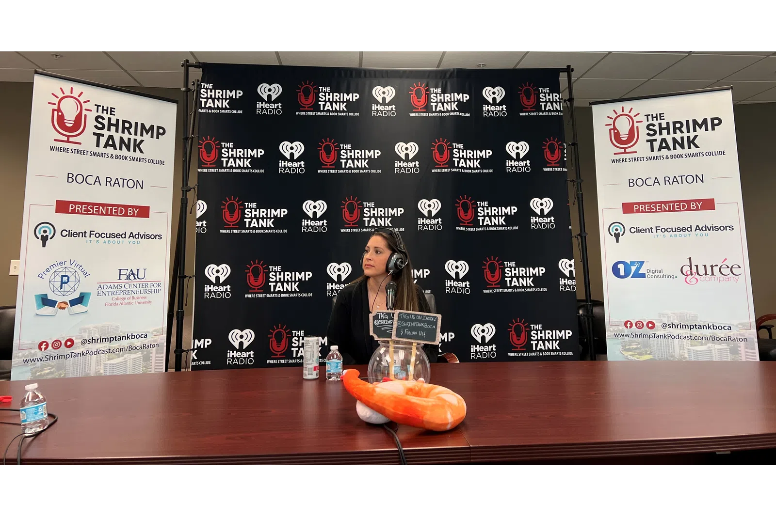 a person sitting at a table with a microphone and a sign behind the