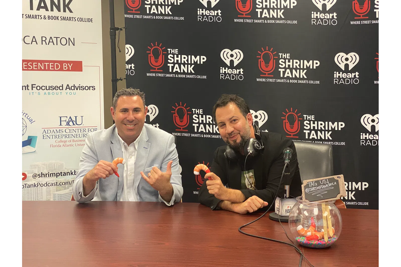 a couple of men sitting at a table with microphones and a sign behind them