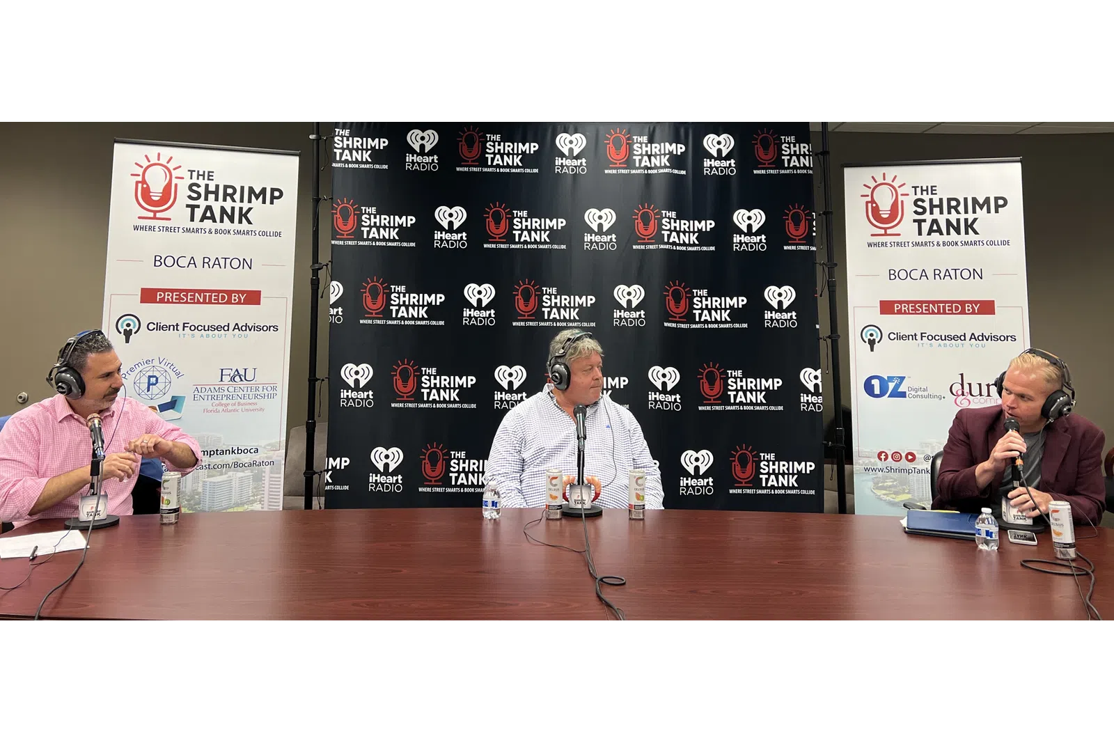 a couple of men sitting at a table with microphones and a sign