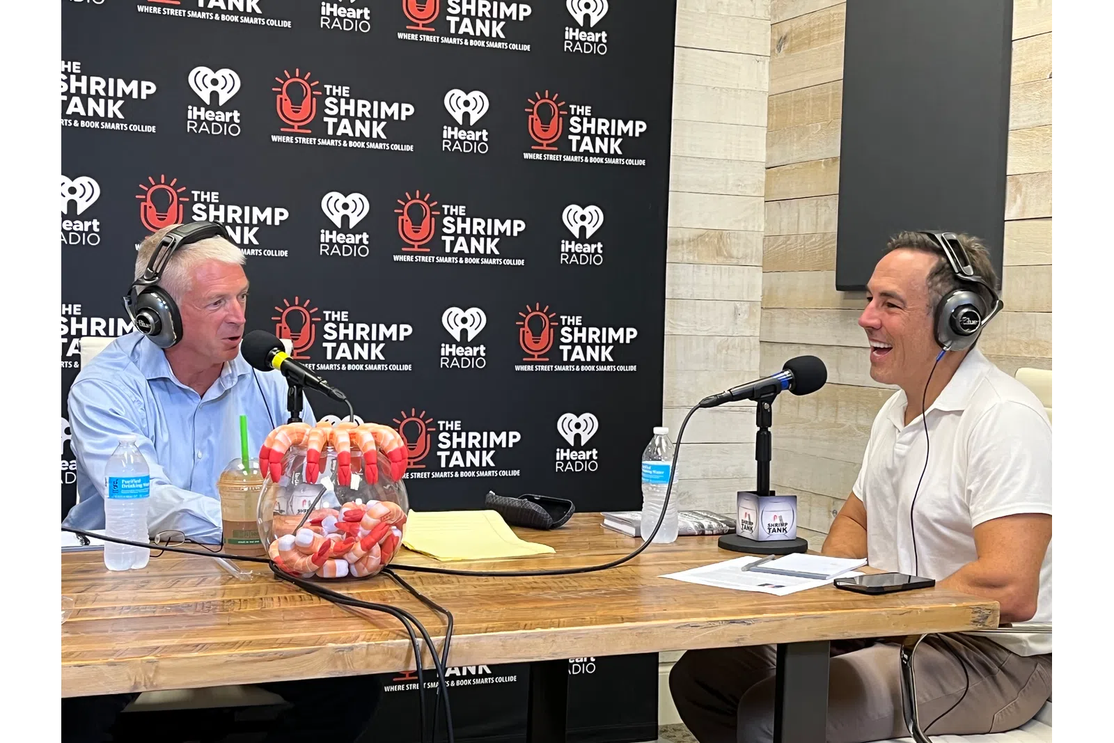 a couple of men wearing headphones and sitting at a table with microphones