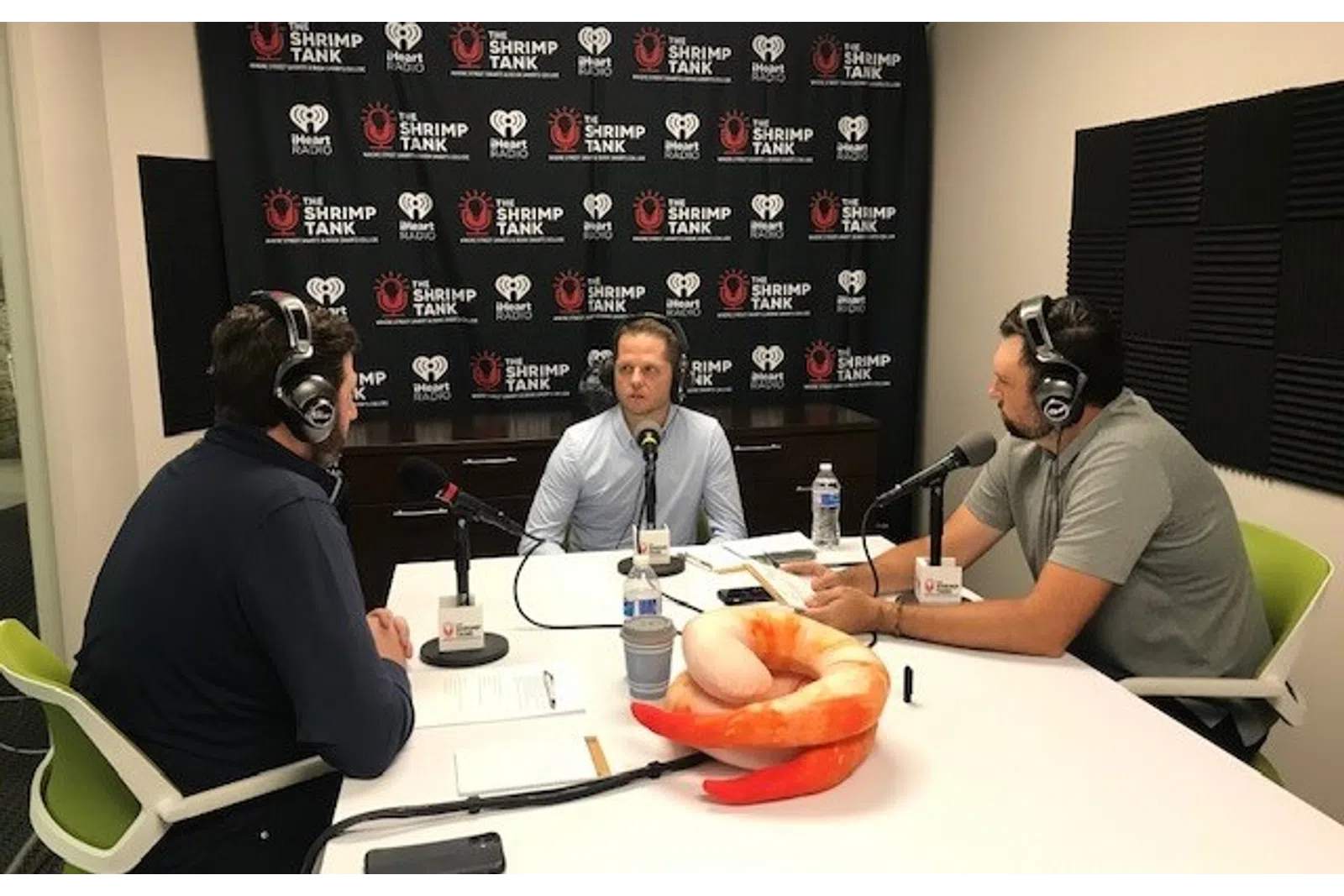 a group of men sitting at a table with microphones and a watermelon