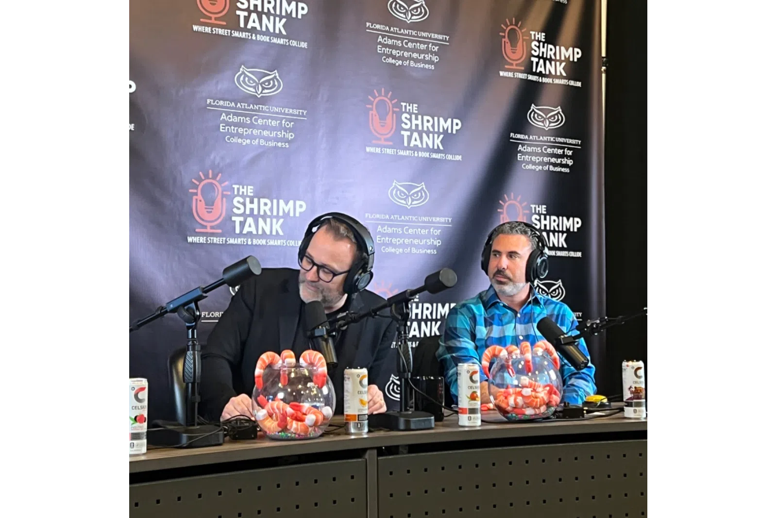 Two men with headphones recording The Shrimp Tank podcast with branded backdrop and shrimp bowls on the desk