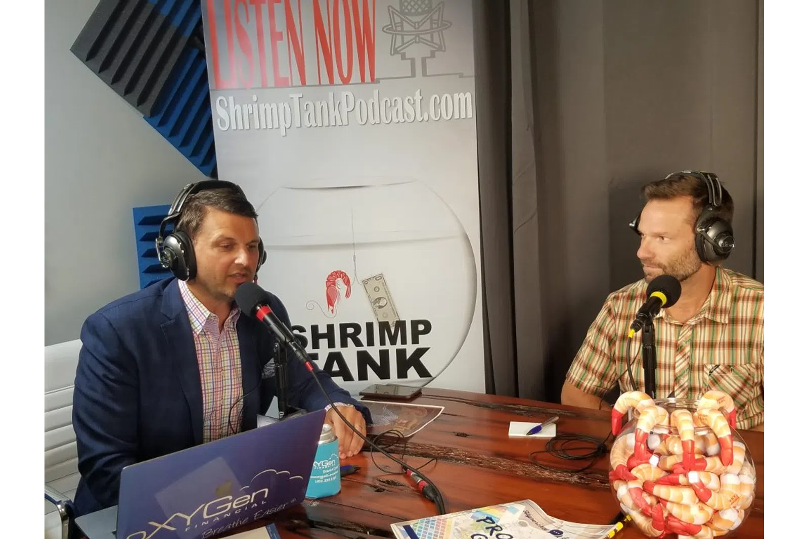 a couple of men wearing headsets and sitting at a table with microphones