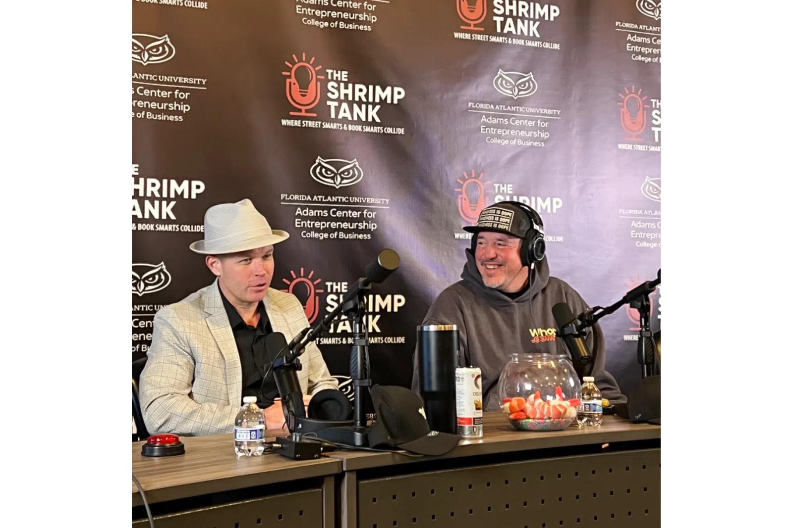 Two men recording a podcast at The Shrimp Tank with microphones and branded backdrop from Florida Atlantic University