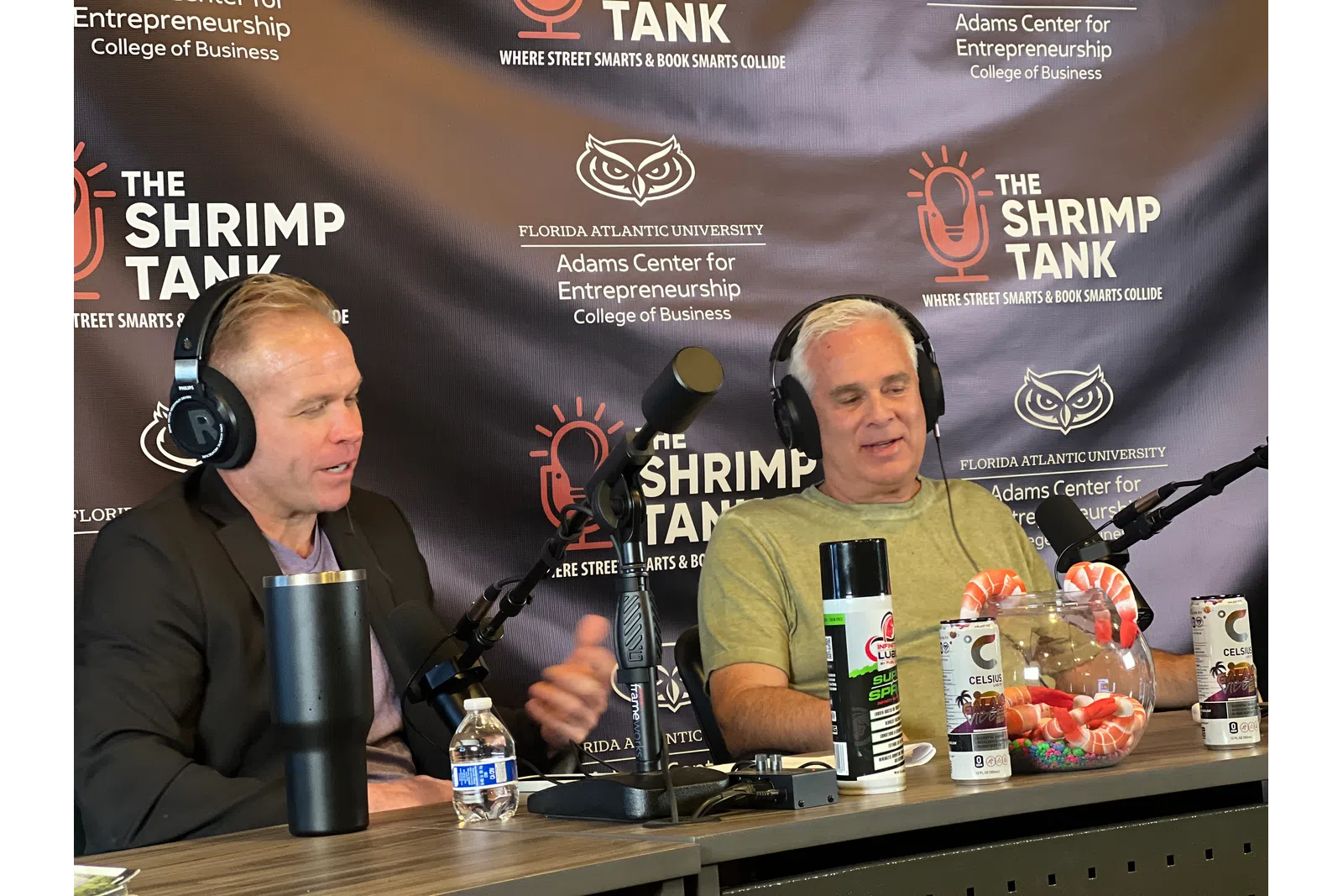 a couple of men sitting at a table with microphones and drinks