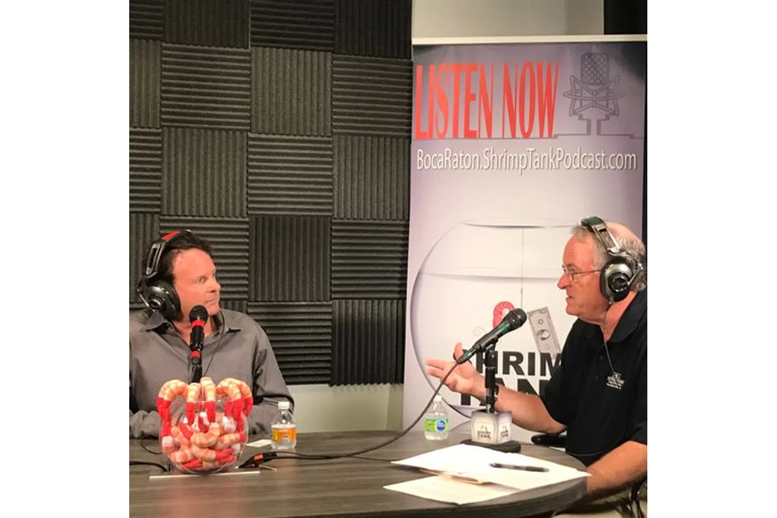 a couple of men wearing headphones and sitting at a table with microphones