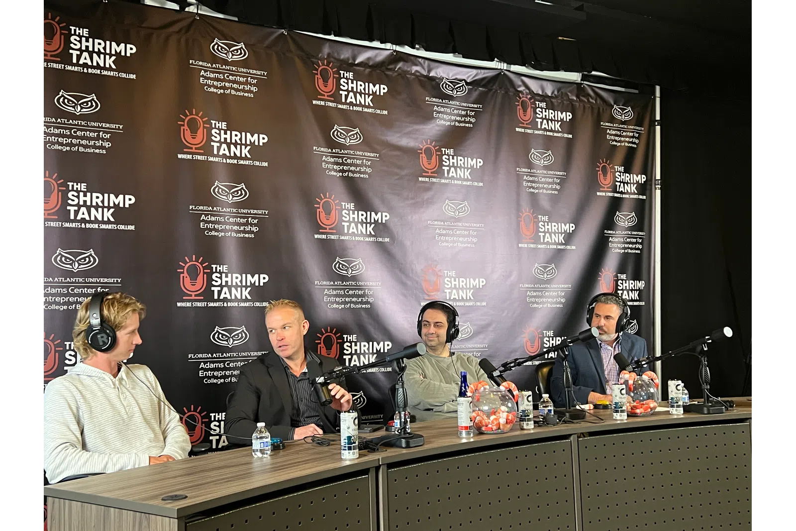 Four men with microphones and headphones sitting at a panel table during The Shrimp Tank event at Florida Atlantic University.