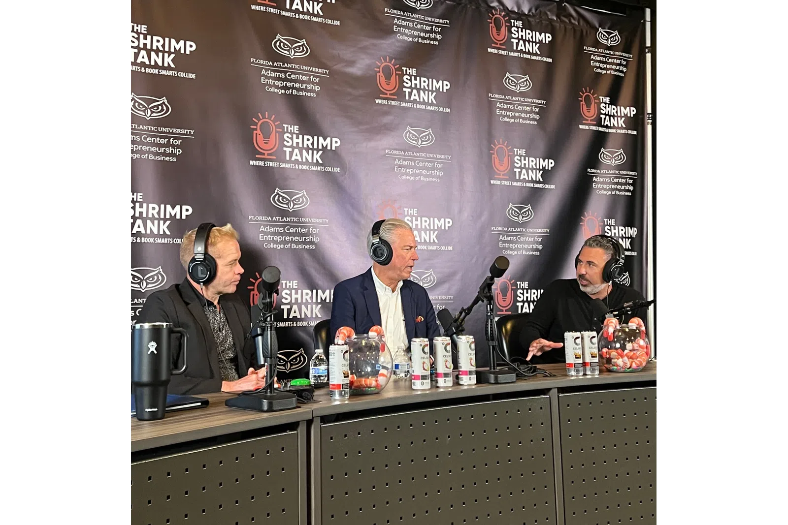 Three men wearing headphones sit at a podcast table with microphones and a The Shrimp Tank branded backdrop.